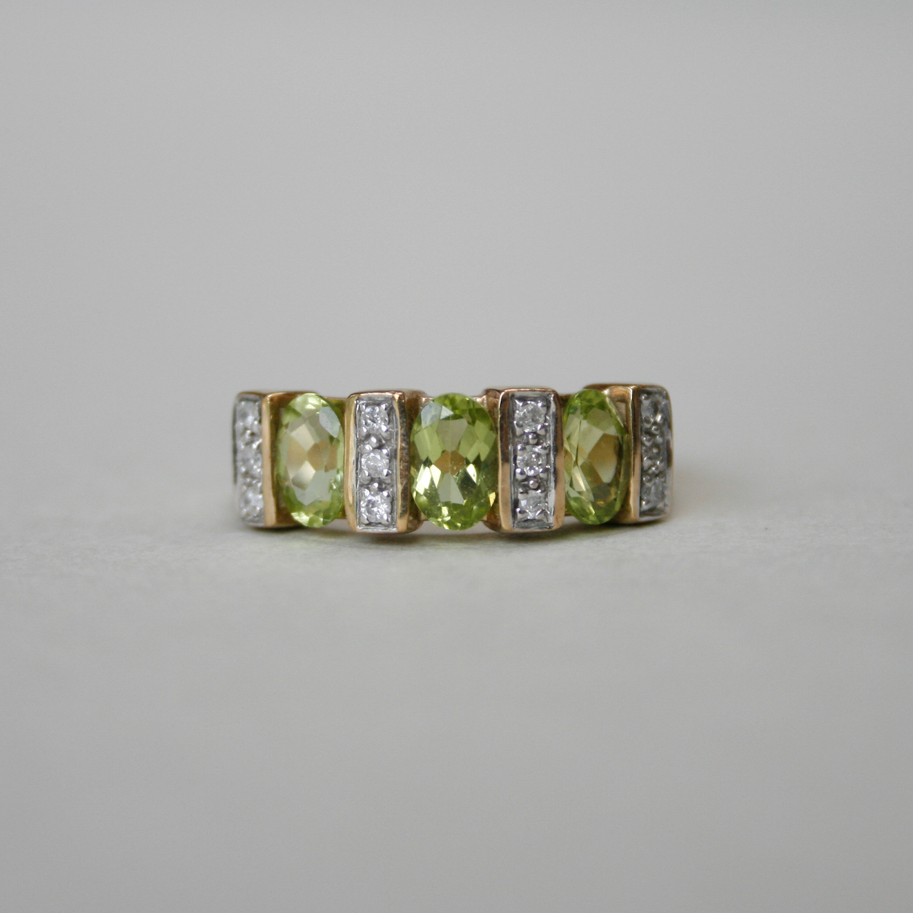 A classic three stone oval peridot and diamond band ring